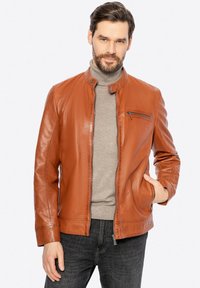 Giacca in pelle marrone con colletto alto, chiusura con zip e tasche laterali. Superficie strutturata, vestibilità slim, indossata sopra un maglione grigio.