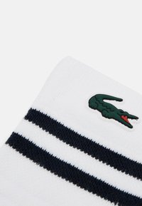 Witte sokken met donkerblauwe strepen, gemaakt van katoen, met een groene krokodillogo-accent. Zachte textuur, gemiddelde dikte.