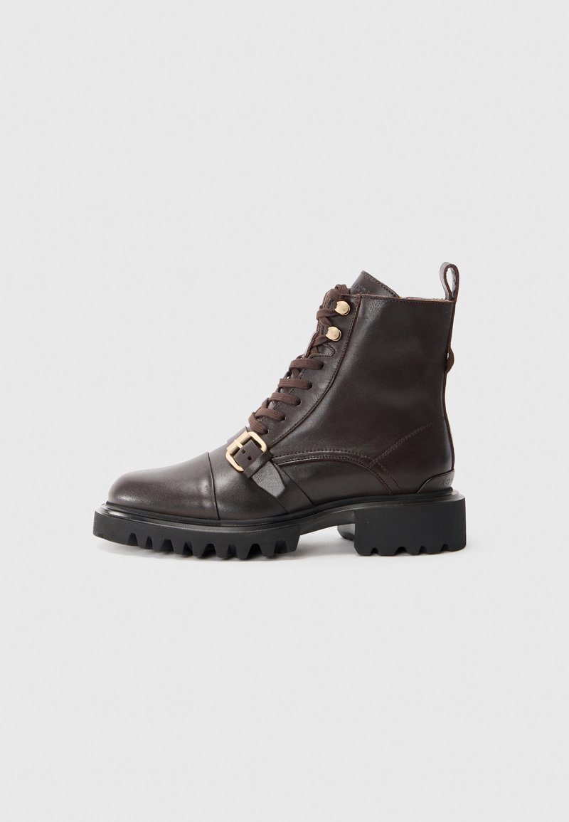 Bottine en cuir marron foncé avec semelle crantée noire épaisse, fermeture à lacets à l’avant et détail boucle dorée sur le côté extérieur.