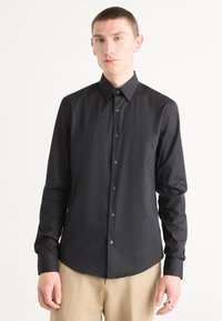 Zwarte langärmelige button-up shirt met een puntige kraag, met een gladde textuur en bijpassende knopen. Gekozen in combinatie met beige broeken.