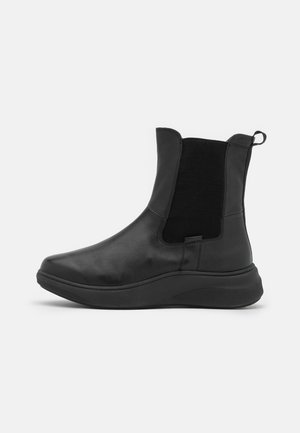 Sort læderankelstøvle med elastisk sidepanel, trækketab og tyk gummisål, vist i profil på hvid baggrund.