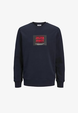 Tumši zils kokvilnas maisījuma džemperis ar apaļu kakla izgriezumu. Tam ir centrāla grafiskā druka sarkanā un melnā krāsā ar uzrakstu "JACK & JONES".