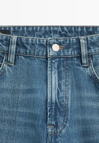 Blå denimjeans med linning, knaplukning, bæltestropper og synlige syningsdetaljer.