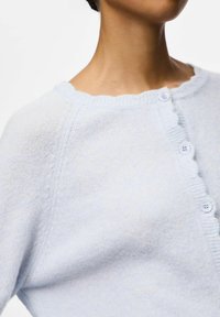 Light blue knitted cardigan with a scalloped neckline, button closure featuring four light blue buttons, and a soft, fine texture.