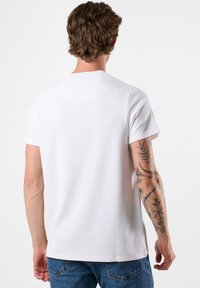 Valkoinen lyhythihainen paita, jossa on teksturoidusta kankaasta valmistettu pyöreä kaulus ja suora helma, yhdistetty sinisiin farkkuihin.