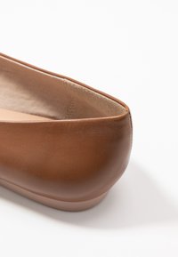 Hnědé kožené baleríny s kulatou špičkou, hladkým povrchem a minimalistickým designem. Uvnitř mají měkkou podšívku.