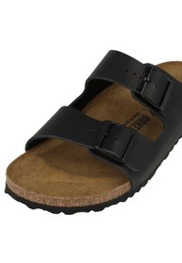 Sandale noire avec deux brides réglables, semelle en liège et semelle en caoutchouc texturée. Matériau lisse avec un logo discret sur les brides.
