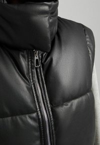 Mustahuuline nahkasärk kõrge kraega, millel on hõbedaste detailidega lukuga esitasku ja diamantruutudega polsterdus. 