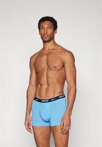 Blaue Baumwoll-Boxershorts mit einem schwarzen Nike-Gummibund, der ein weißes Logo trägt. Der Stoff wirkt glatt und das Design ist körperbetont.