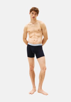 Boxer ajustados negros hechos de un tejido suave, con una cintura de color gris claro que lleva el logo "TOMMY HILFIGER". El diseño incluye una forma que se ajusta al cuerpo.