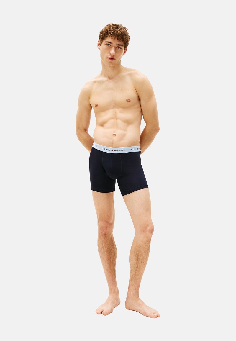 Boxer ajustados negros hechos de un tejido suave, con una cintura de color gris claro que lleva el logo "TOMMY HILFIGER". El diseño incluye una forma que se ajusta al cuerpo.