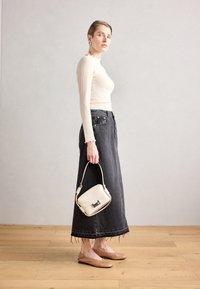 Cremfarbener Langarm-Top mit gerippter Textur, schwarzer Jeansrock mit ausgefranstem Saum, beigen Ballerinas und einer kleinen weißen Handtasche mit silbernem Akzent.