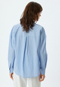 Lichtblauw gestreept shirt met een ontspannen pasvorm, voorzien van een rugplooitje, knoopmanchetten en een afgeronde zoom. Glad stoftextuur.