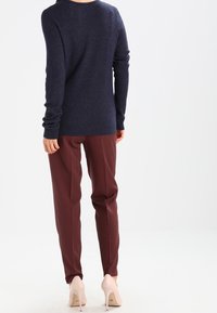 Marinblå tröja med långa ärmar, ribbade manschetter och fåll; tillsammans med vinröda skräddarsydda byxor och beige högklackade skor, sedd bakifrån.