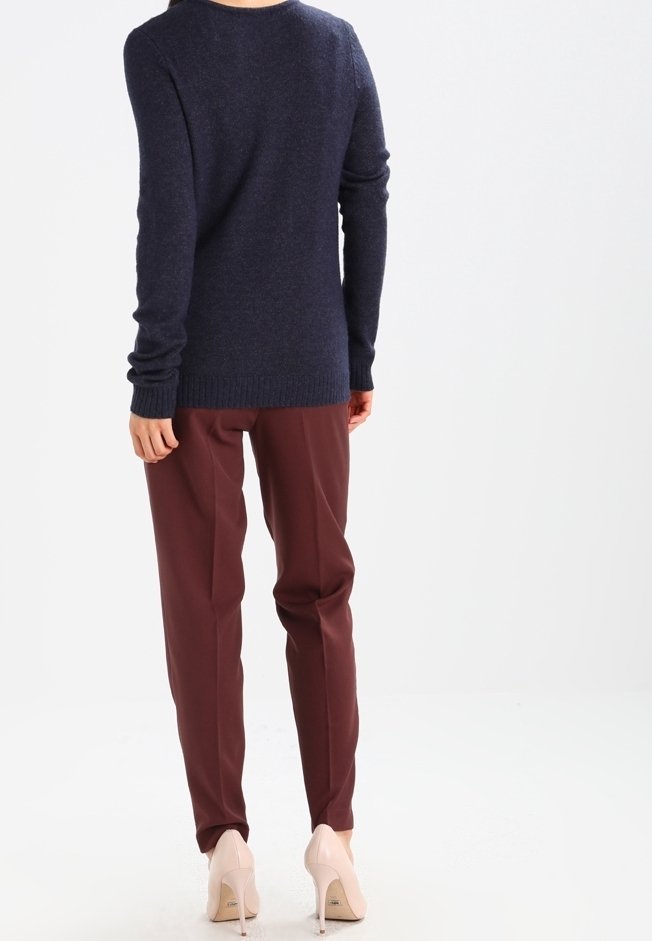 Marinblå tröja med långa ärmar, ribbade manschetter och fåll; tillsammans med vinröda skräddarsydda byxor och beige högklackade skor, sedd bakifrån.