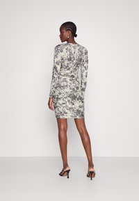 Robe mini à manches longues et près du corps en tie-dye vert et gris. Présente une taille froncée et un tissu texturé, associée à des talons noirs.