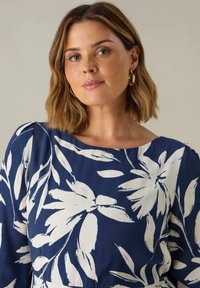 Námořnické šaty s bílým květinovým vzorem, mají čtvercový výstřih, dlouhé rukávy a měkkou texturu tkaniny.