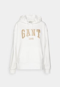 Sudadera blanca con un gran logotipo bordado en dorado "GANT" y "1949" debajo, con un bolsillo frontal y capucha ajustable. Textura de tela suave.