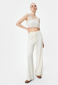 Top court blanc avec un motif en maille texturée et ouverte, associé à un pantalon ample couleur crème doté d'une taille élastique et d'un cordon de serrage.