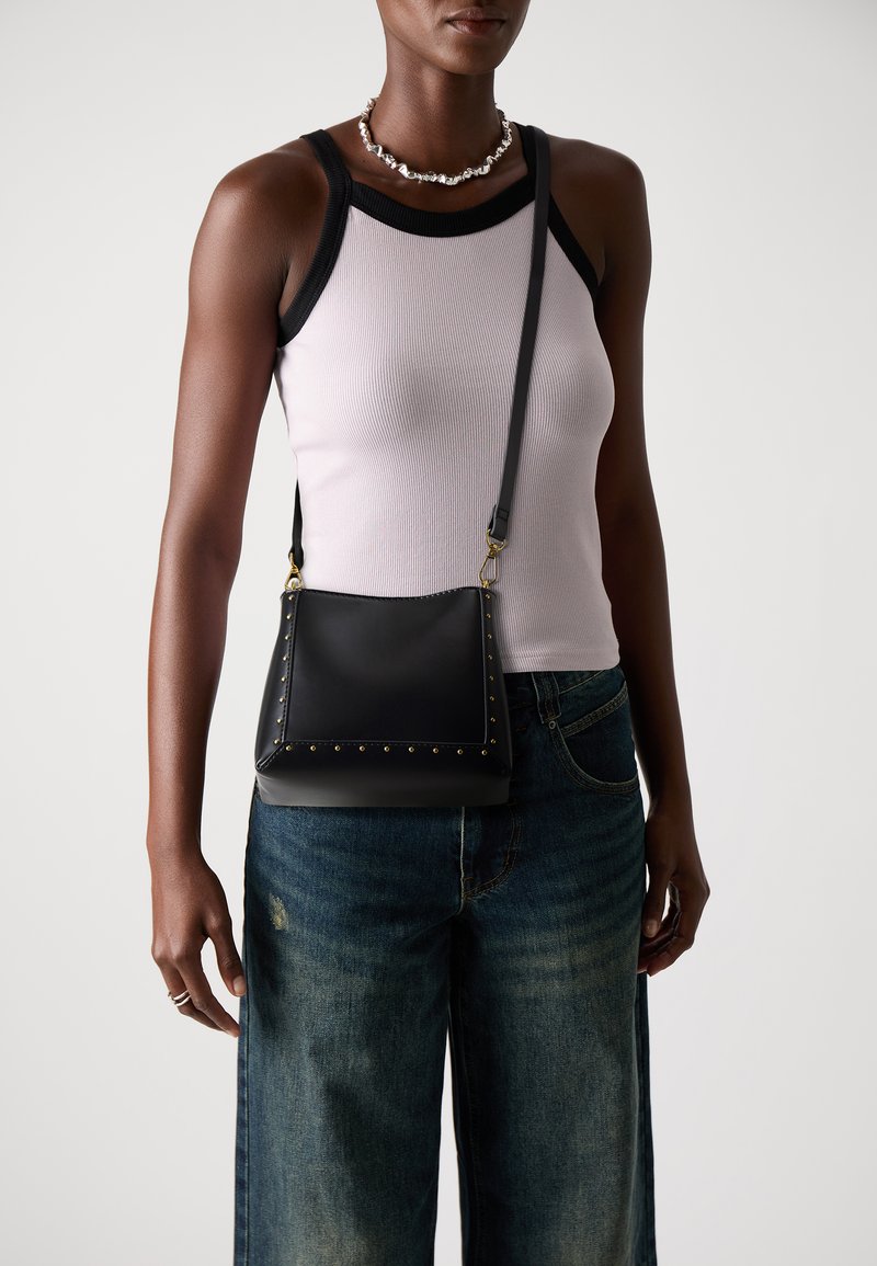 Sac en bandoulière en cuir noir avec des clous dorés sur le bord, doté d'un design plat et d'une sangle ajustable. S'associe avec un denim décontracté.