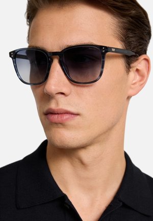 Occhiali da sole con montatura nera trasparente, lenti scure sfumate, forma rettangolare e un accento sottile vicino alle cerniere; design minimalista.