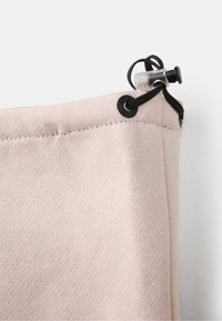 Saco de cordão de cor rosa claro, com tecido texturizado, apresentando acessórios em preto e um fecho de aperto na parte superior. Material suave e flexível.