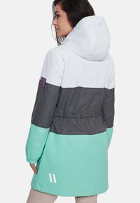 Moteriška spalvų derinimo striukė balta, pilka ir mėtų žalia. Pasižymi kepure, elastinga juosta juosmeniui ir purpuriniu miesto stiliaus lopu ant rankovės.