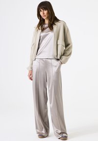Chaqueta bomber de un gris claro y esponjoso sobre una blusa de satén plateado y pantalones anchos de satén, con líneas limpias y una textura suave.