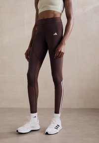 Bordo tajice s bočnim panelima i tri bijele pruge, uparen s bijelim sportskim tenisicama i čarapama do gležnjeva. Sportski grudnjak u svijetlozelenoj boji.