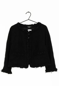 Chaqueta negra texturizada con un corte corto. Presenta un dobladillo deshilachado, un ribete rizado a lo largo del escote y dos bolsillos frontales.