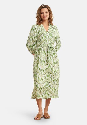 Groene en witte jurk met een V-hals, lange mouwen en een tailleband. Stof met een bloemig bladdessin; middenlang.