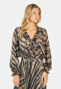 Blusa transparente con escote con volantes, detalles de botones y mangas largas en un patrón de rayas en tonos marrones y grises. Tejido ligero.