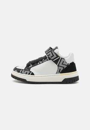 Black and white sneaker featuring a textured leather and suede upper, geometric pattern details, and a hook-and-loop strap. Flat rubber sole.