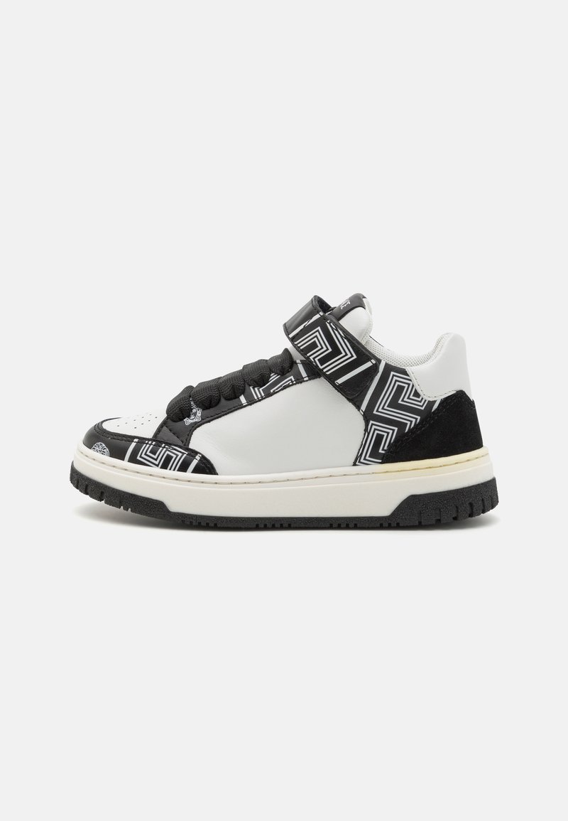 Svart och vit sneaker med ett ovansidan i texturerat läder och mocka, geometriska mönsterdetaljer och ett kardborreband. Platt gummisula.