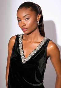 Čierny zamatový top s výstrihom do V, ozdobený dekoratívnym strieborným korálkovým pásom. Hladký povrch, bez rukávov.