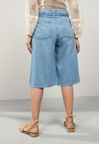 Világoskék farmer culottes magas derékkal, széles lábszárakkal és két hátsó zsebbel, barna pántos szandállal párosítva.