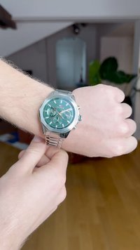 Silver metal watch with a textured green dial, three chronograph subdials, and a polished stainless steel band, worn on a wrist.
