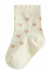 Cream-colored sock with a ribbed cuff and soft texture, featuring a pattern of small, scattered tan hearts throughout.