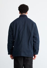 Navyblaue Jacke aus leichtem Material, mit Kragen und weiten Ärmeln, glatter Textur und einfachen, klaren Linien.