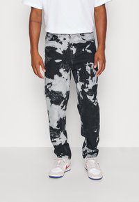 Vaqueros de tie-dye en blanco y negro con un corte relajado, que presentan un diseño clásico de cinco bolsillos y costuras visibles, combinados con zapatillas blancas.