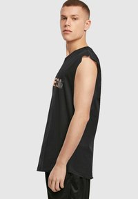 Melnā bez piedurknēm T-krekls ar noapaļotu kakla izgriezumu un izgrieztiem pleciem. Priekšpusē ir daudzkrāsains grafisks teksts.