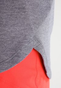 Tissu en maille grise avec une finition texturée, doté d'un ourlet incurvé, associé à un matériau rouge vif en dessous, mettant en valeur le contraste des couleurs.