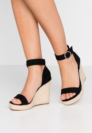 Zwarte suède wedge sandalen met enkelband en zilveren hardware, met een gegoten platformzool van textuur jute.