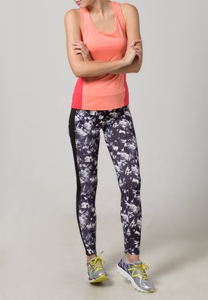 Un débardeur de sport corail associé à des leggings à motifs noir et blanc. Des baskets avec des accents gris et jaune, et des semelles texturées.