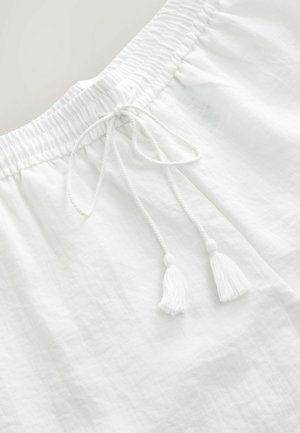 Valged linased lühikesed püksid elastse vöökoha ja reguleeritava paelaga, millel on kaks valget tupsu, ning tekstuuriga pind.