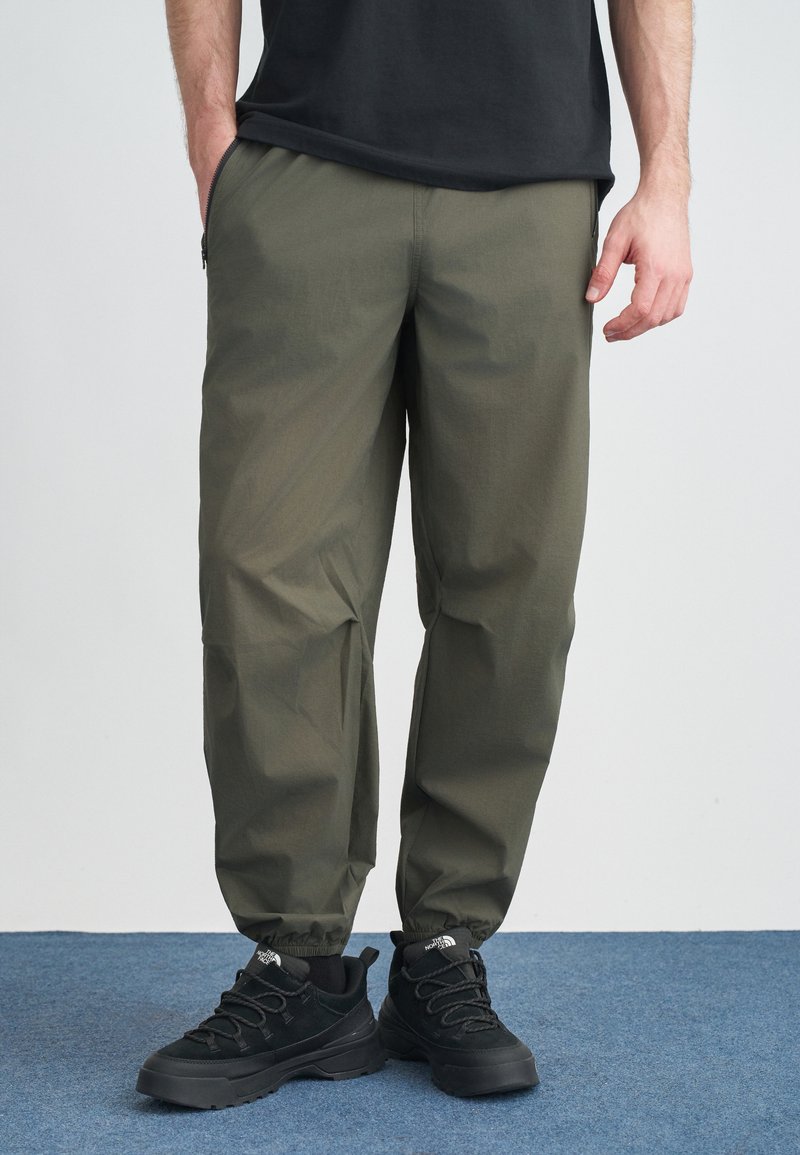 Ελαφριά παντελόνια σε ελιά πράσινο με άνετη εφαρμογή, ελαστικά τελειώματα και πλαϊνές τσέπες, συνδυασμένα με μαύρα, υφή αθλητικά παπούτσια.