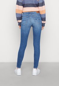 Úzké modré džíny vyrobené z denimu, s mírně zvýšeným pasem, dvěma zadními kapsami a jemně vybledlou texturou. V kombinaci s bílými teniskami.