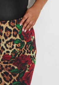 Falda de tela de estampado de leopardo con rosas rojas y hojas verdes, textura suave, diseño ajustado, con una parte superior negra parcialmente visible.