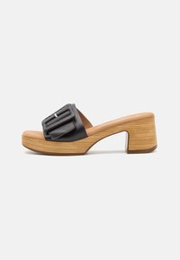 Svart skinnsandal med bred rem som har en rektangulär spänne, placerad på en robust, träblockklack med en strukturerad yta.