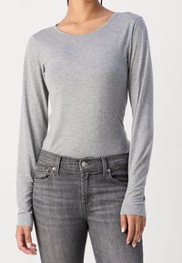 Graues Langarm-T-Shirt mit runder Ausschnitt, aus einem weichen, leichten Stoff, kombiniert mit dunkelgrauen, figurbetonten Jeans.